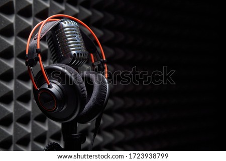 Studio condenser microphone with professional headphones on acoustic foam panel background, copy space on right