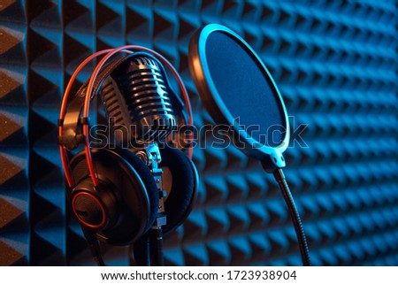 Studio condenser microphone with professional headphones and pop-up filter, on acoustic foam panel background with orange side light, copy space on right