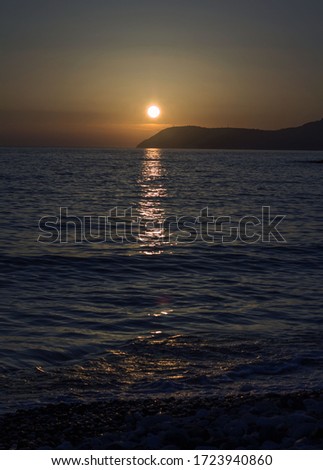 Sea sunset, where the yellow disk of the sun reflects a white path on the water.