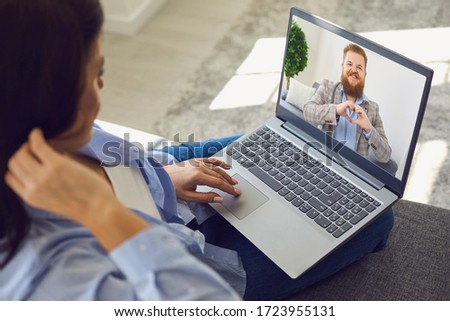 Date online. Loving couple. Funny man looking at the camera smiling holds his hands in the shape of a heart video chat call using laptop at home.
