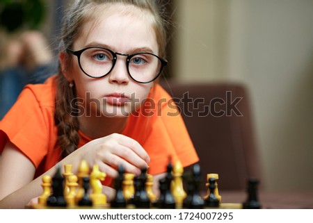 Portrait of a small Caucasian girl with glasses playing chess at home during quarantine due to coronavirus