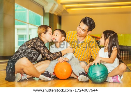 Asian family activity concept : Group of parents, sons and daughters participated in recreational activities, bowling, sitting together, and smelling their sons with happiness : Selective Focus 
