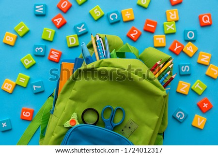 Back to school concept. Backpack with school supplies and alphabets and numbers blocks on blue background. Top view. Copy space