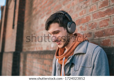 Portrait of young latin man listening to music with headphones against brick wall. Urban concept. Royalty-Free Stock Photo #1724023852