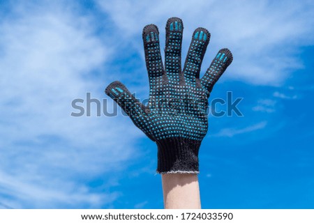 a hand in a working black glove shows signs and gestures against the background of blue sky and white clouds on the street in the summer on fresh water
