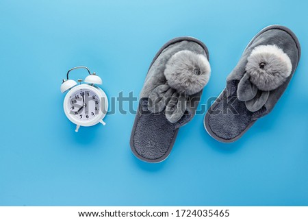 White alarm clock and slippers on blue background. The concept of good morning and morning ritual.