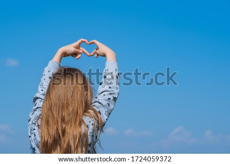 Little girl made a heart with her fingers against the blue sky.love Concept, Heart-shape hand gesture.