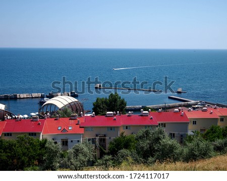 view of the blue sea and cottages with red roofs on the shore near the club's yachts