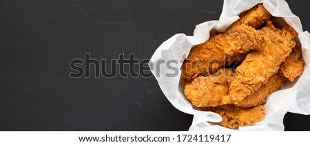 Homemade chicken fingers in paper box on a black background, top view. Flat lay, overhead, from above. Space for text. Royalty-Free Stock Photo #1724119417