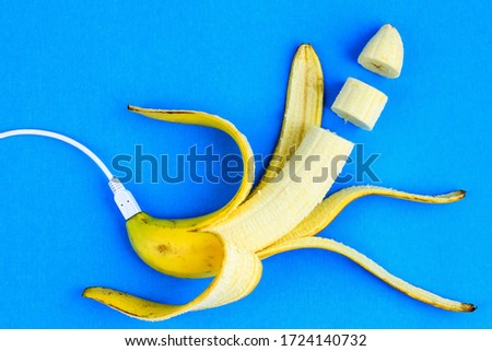 A fresh ripe banana connecting with a white usb charge cable. Creative concept of alternative electricity source, battery charger indicator, energy, healthy food.