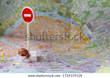 Tiny snail with horns crawls around a forbidding sign on the city map background