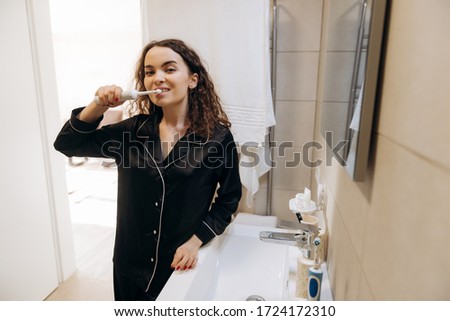 Portrait of a beautiful woman brushing teeth and looking in the mirror in the bathroom