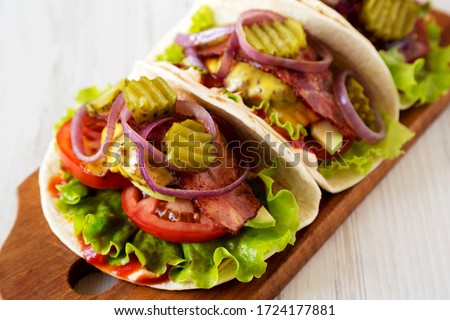 Homemade Bacon Cheeseburger Tacos on a rustic wooden board on a white wooden background, low angle view. Close-up.