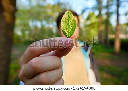 Young man holding green leaf in front of face, save the earth concept.