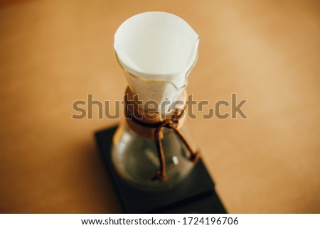 Preparing for alternative coffee brewing v60. Fold coffee filter. Folding paper filter in pour over and glass kettle on scale on brown background. Royalty-Free Stock Photo #1724196706