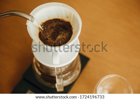 Pouring hot water from steel kettle in filter with ground coffee in pour over on scale. Alternative coffee brewing v60 closeup. Barista making filter coffee on brown background Royalty-Free Stock Photo #1724196733