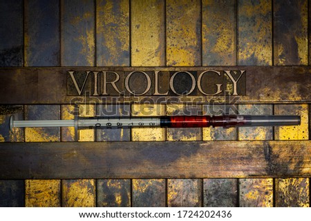 Photo of real authentic typeset letters forming Virology text with red fluid filled syringe on vintage textured grunge copper background