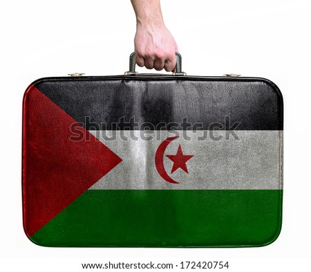 Tourist hand holding vintage leather travel bag with flag of Western Sahara