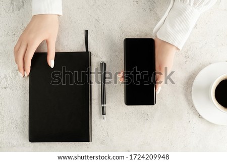 Beautiful women's hands with up-to-date smartphone, notebook, fountain pen and cup of coffee on concrete background. Women's business concept. Coffee break top view. Mockup for your design.