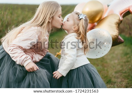 Two little sisters in luxurious dresses with balloons on a background of green field. daughter's day