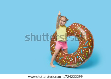 Failed summer vacation. Happy surprised child model girl resting on a donut-shaped rubber ring. Sea vacation concept on a colored blue background. 