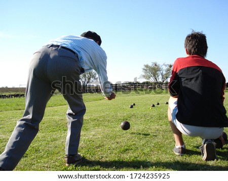 Playing bowls on the field. Two men play on the grass during the day and in sunlight.                  