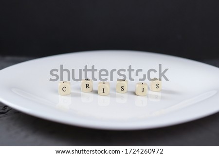 The word crisis, which is assembled from cubes in the foreground and an empty, white plate. Copy space - concept of economic problems, hunger.