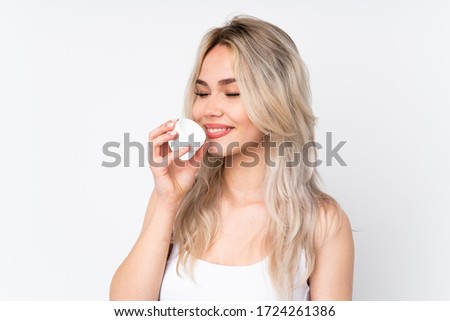 Teenager blonde girl over isolated white background with moisturizer and smelling it