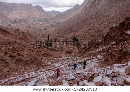 Hikers on the hiking trail  in the remote region of the Southern Sinai. Panoramic view over the trail on surrounding red mountains and valley with bedouin settlement Saint Catherine on the background.