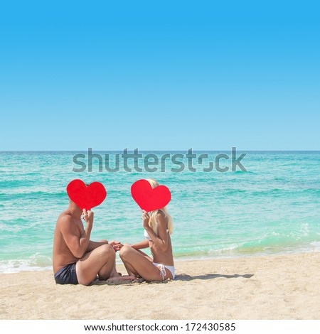 Loving couple at sandy sea beach with red hearts - St. Valentines Day concept