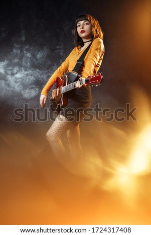 Pretty young hipster woman with curly hair with red guitar in neon lights. Rock musician is playing electrical guitar.