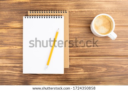 Spiral notebook with pencil and coffee cup on a wooden background. Design concept with copy space for notes. Blank page for business text. Office notepad. Top view.