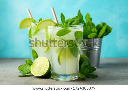 Two homemade lemonade or mojito cocktail with lime, mint and ice cubes in a glass on a light stone table. Fresh summer drink