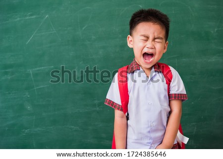 Back to School. Happy Asian funny cute little child boy from kindergarten in student uniform with school bag stand smiling on green school blackboard, First time to school education concept
