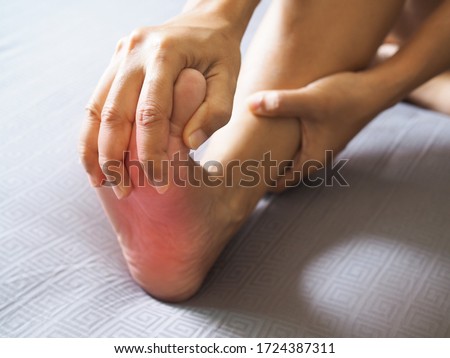 People sitting in bed with foot pain use hand to massage toe, leg, ankle and soles to relax and relieve pain.