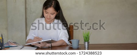 Cropped shot of female university student drawing on digital tablet while doing her project with stationery and designer supplies on worktable