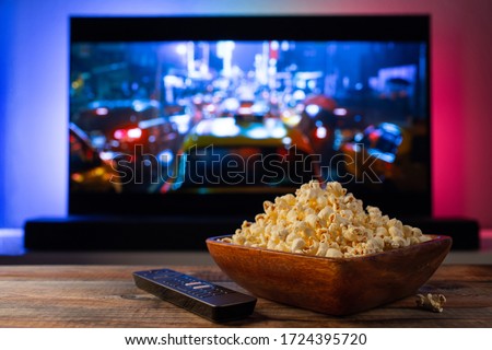 A wooden bowl of popcorn and remote control in the background the TV works. Evening cozy watching a movie or TV series at home Royalty-Free Stock Photo #1724395720