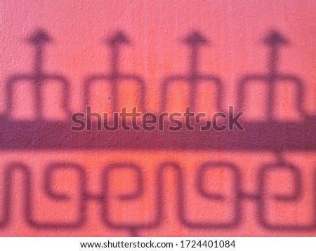The shadow of a stainless steel fence on a red concrete wall. Chinese style stainless steel fence. Thai and chinese design together.
