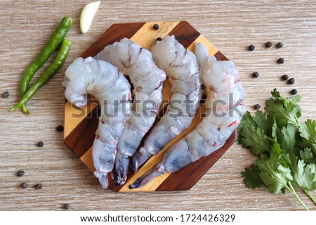 Cleaned, Peeled & Deveined Tiger Prawns or Asian tiger Shrimps. Also known as Kolambi or Bagda chingri. Recipe ingredients like pepper, chilies, garlic, curry leaves at background with copy space.  Royalty-Free Stock Photo #1724426329