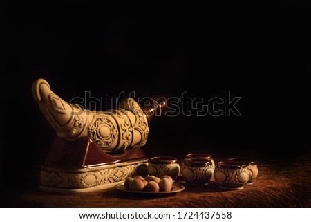 A closeup shot of a dagger-shaped bottle, decorated cups and a pile of chestnuts placed on a table in a dark and warm setting