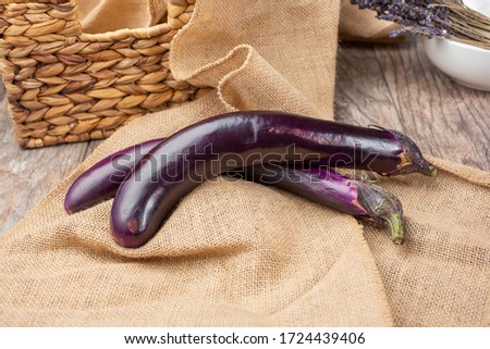A view of two Japanese eggplants on pile of burlap, in a still life setting.
