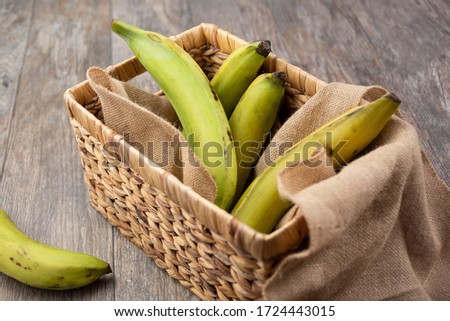 A view of several unripened green plantains in a basket, in a still life setting.