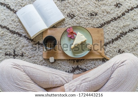 A girl enjoys a relaxing tea and cake while reading a book sitting on on a cosy Moroccan wool Beni Ourain rug. Royalty-Free Stock Photo #1724443216