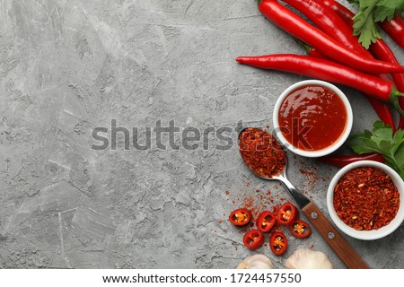 Composition with chilli pepper, powder spice, garlic and sauce on gray background Royalty-Free Stock Photo #1724457550