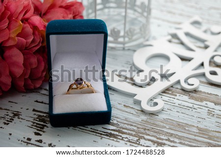 Gold ring in the aquamarine gift box with pink flowers on the white wood background. Symbol of love
