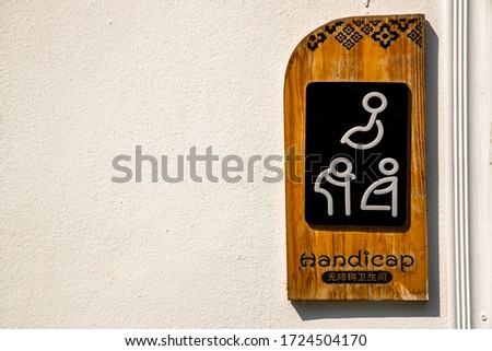 Translation: For handicapped people.
Toilet sign for handicapped people, pregnant women and the elderly with illustration on wooden panel against white concrete wall.