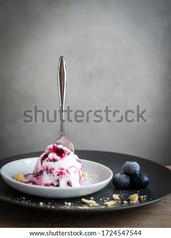 A scoop of blueberry ice cream and a rustic spoon on a gray plate, close-up, frozen fruit, ice cream, summer, ready to serve