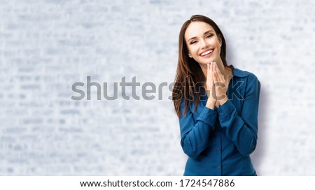Portrait of happy toothy smiling woman holding clasp hands near mouth, standing over white brick wall background. Optimistic, positive, happy feeling and dental health concept picture. 