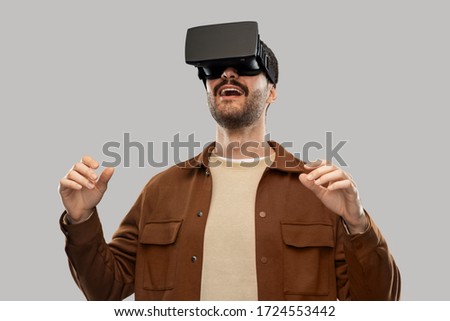 future, technology and people concept - happy smiling young man with mustaches in virtual reality headset or vr glasses over grey background