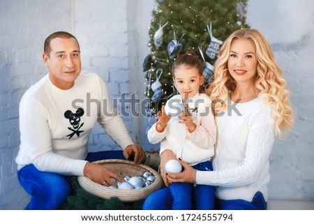 Cute family at home. Beautiful blonde mother, father and little daughter in white sweaters at home in bedroom with christmas decorations and xmas tree on background. Fun, trust and love. Home concept.